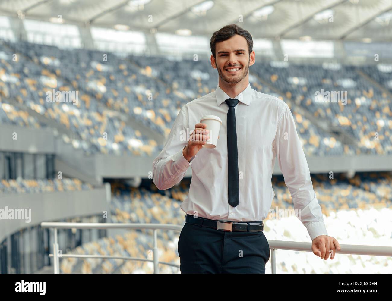 Lächelnder Unternehmer, der Kaffee trinkt, während er auf der Aussichtsplattform des Stadions steht Stockfoto