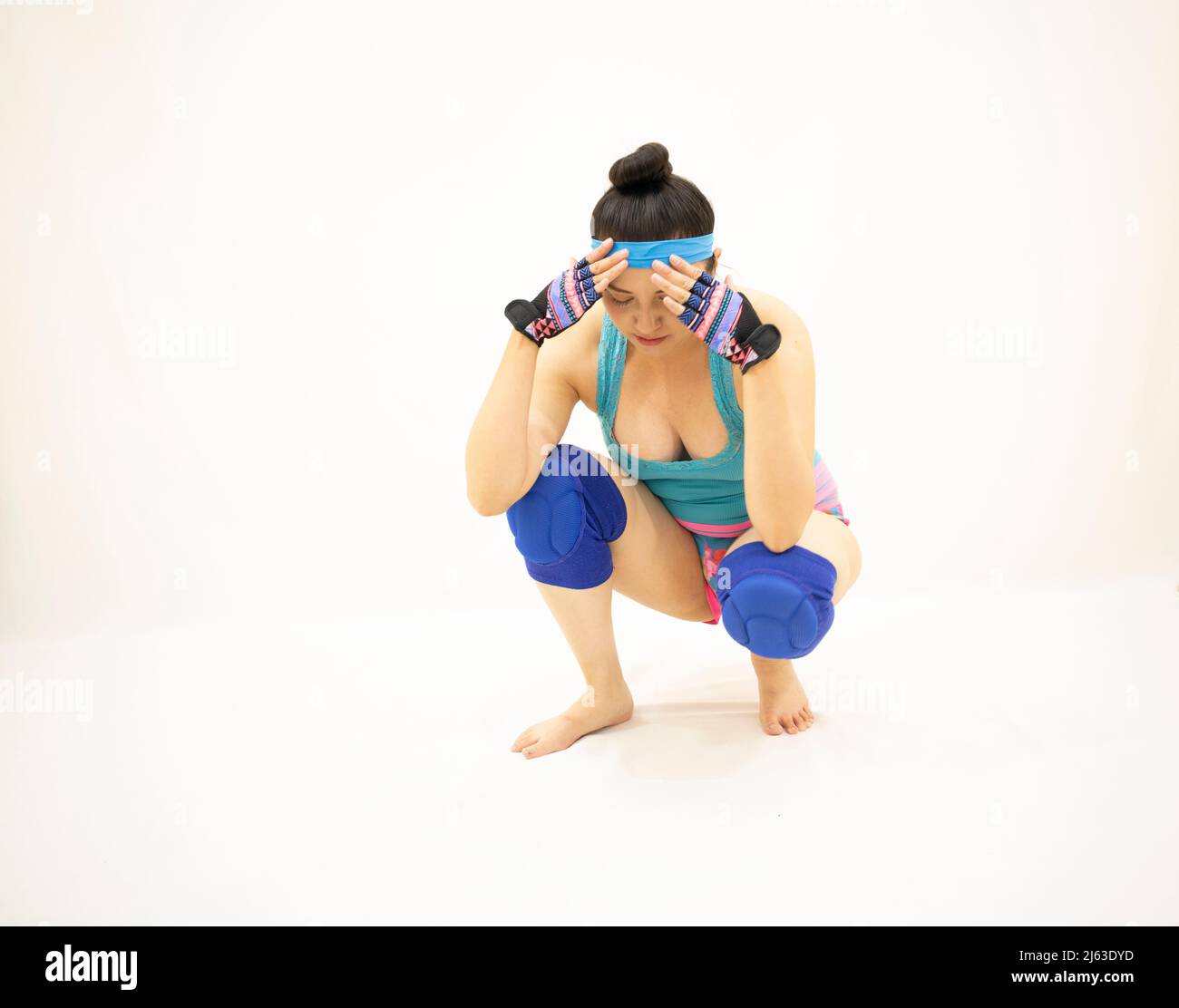 Frustrierte, athletische Frau, die mit den Händen auf ihrem Kopf hockt und blaue Knieschoner und Handschuhe trägt Stockfoto