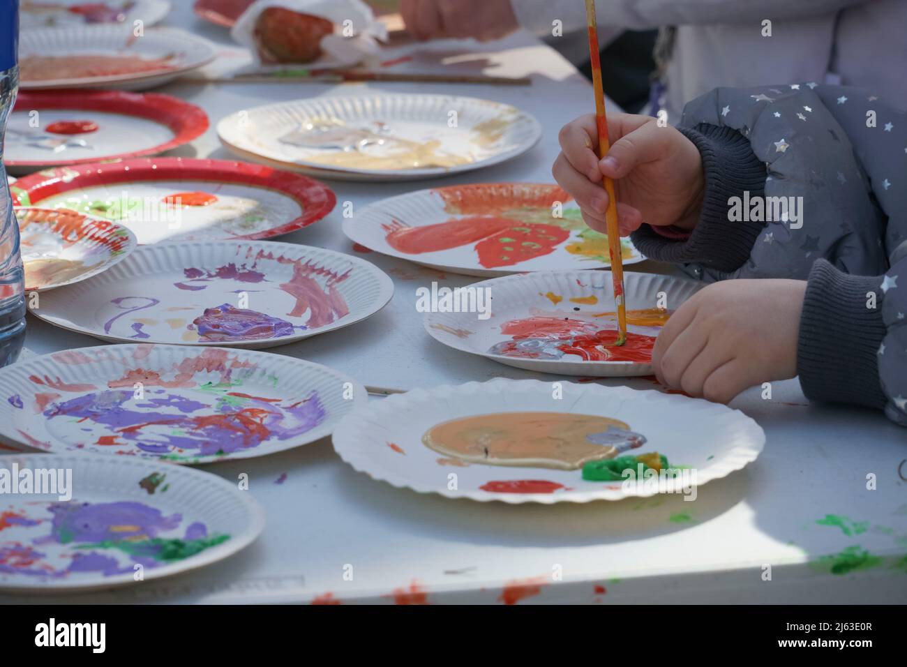 Kinder malen mit Farben. Outdoor-Farb-Kreativworkshop für Familien mit Kindern im Frühling zur Osterfestzeit. Geschirr auf dem Tisch mit den Farben. Stockfoto