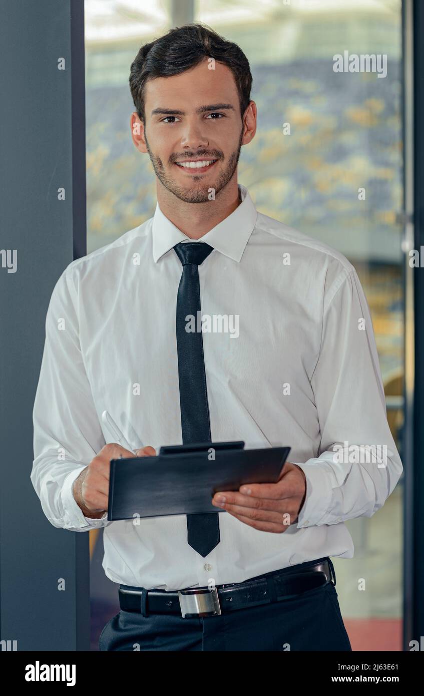 Hübscher junger Geschäftsmann in weißem Hemd, der Tablet mit Papieren hält Stockfoto