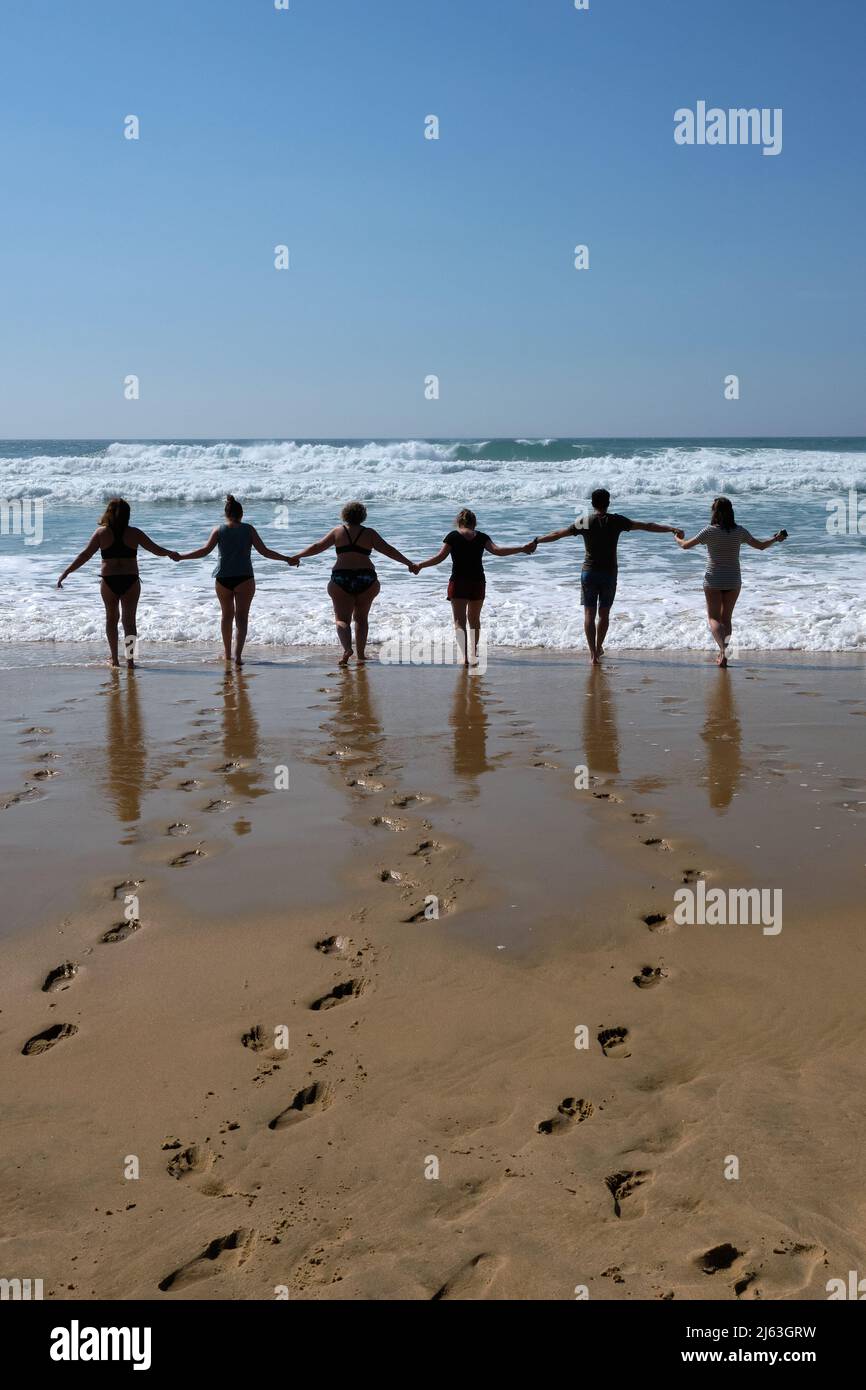 Vertikale Aufnahme einer Gruppe von Freunden, die die Hände an einem Strand halten, der zum Meerwasser geht. Stockfoto