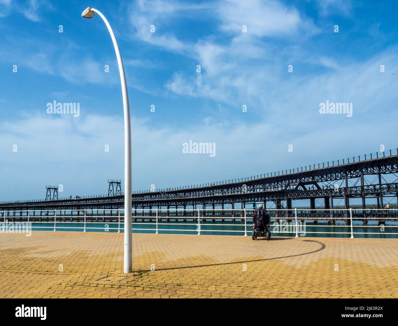 Ein älterer Mann im Rollstuhl genießt an einem sonnigen Tag einen Spaziergang entlang des Flusses Odiel in Huelva. Stockfoto