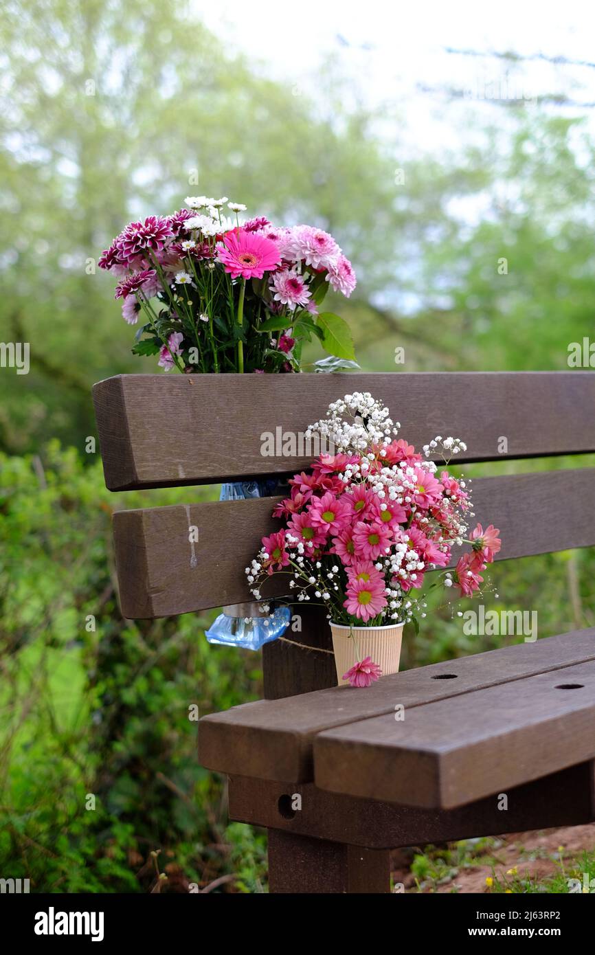 Blumen, die in Erinnerung an einen geliebten Menschen auf einer Bank zurückgelassen wurden. Stockfoto