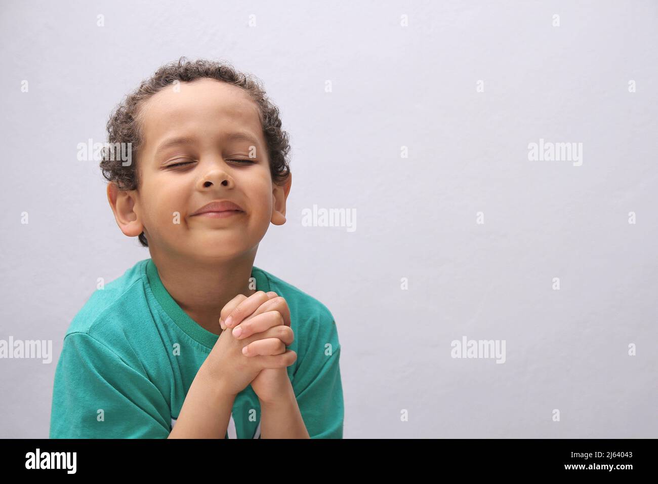 Ein kleiner Junge betet zu Gott mit Händen zusammen mit einem schwarzen Hintergrundfoto Stockfoto