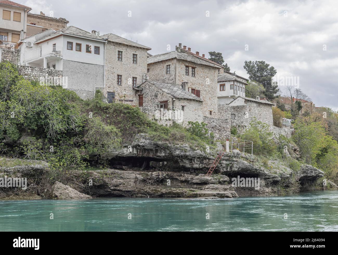 Blick über einen türkisfarbenen Fluss auf Gebäude an einem Flussufer und einige Stufen, die zu einigen Felsen führen Stockfoto