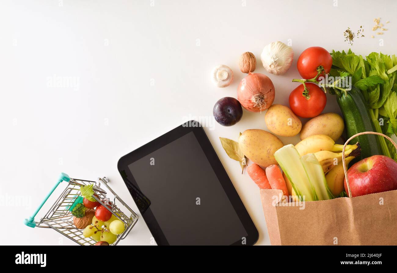 Konzeptioneller Hintergrund des Online-Einkaufs mit mobilen Geräten und Supermarkt-Einkaufstasche voller Obst und Gemüse. Draufsicht. Horizont Stockfoto