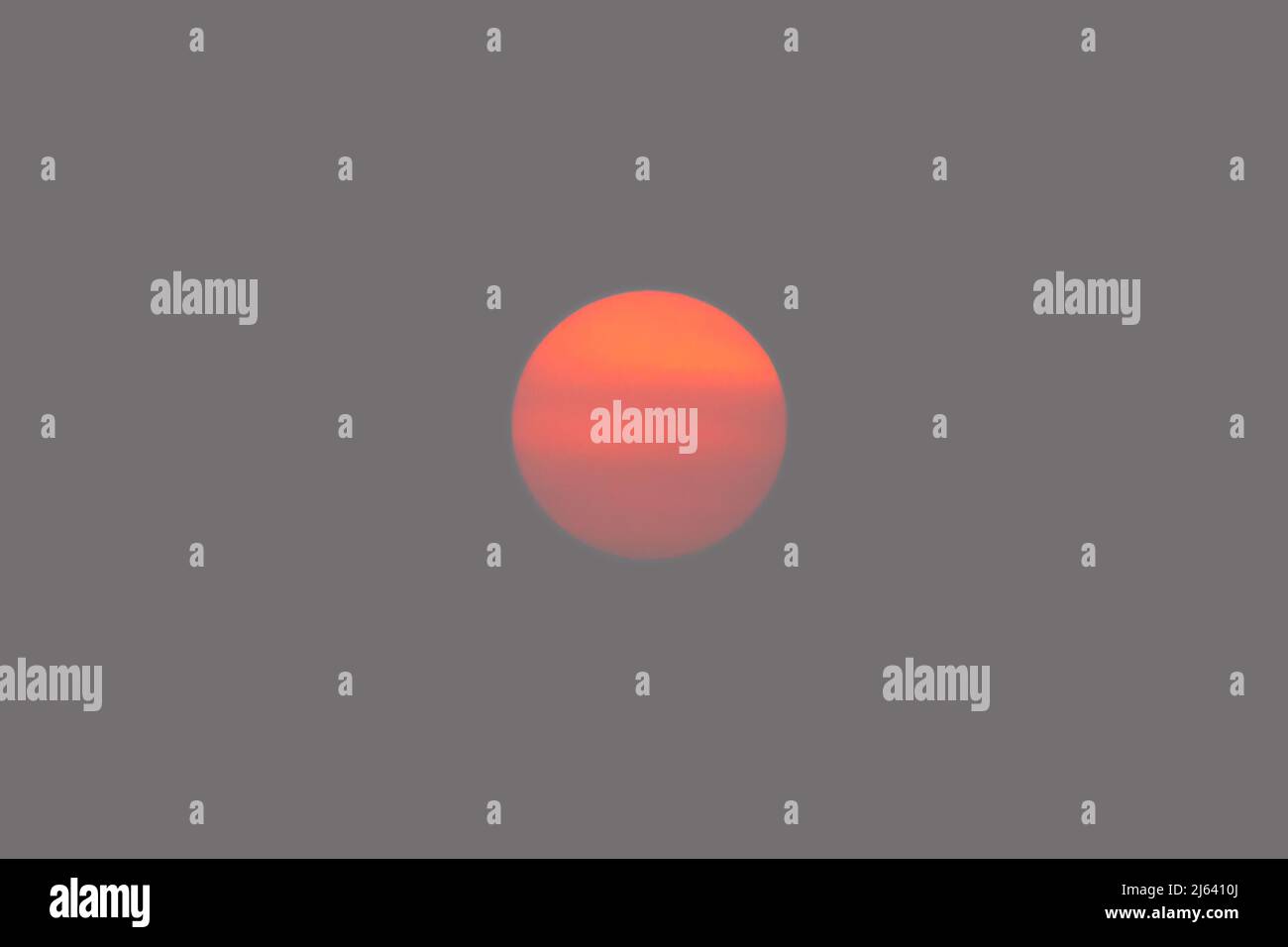 Orangefarbene Sonnenscheibe isoliert am rauchigen Himmel Stockfoto