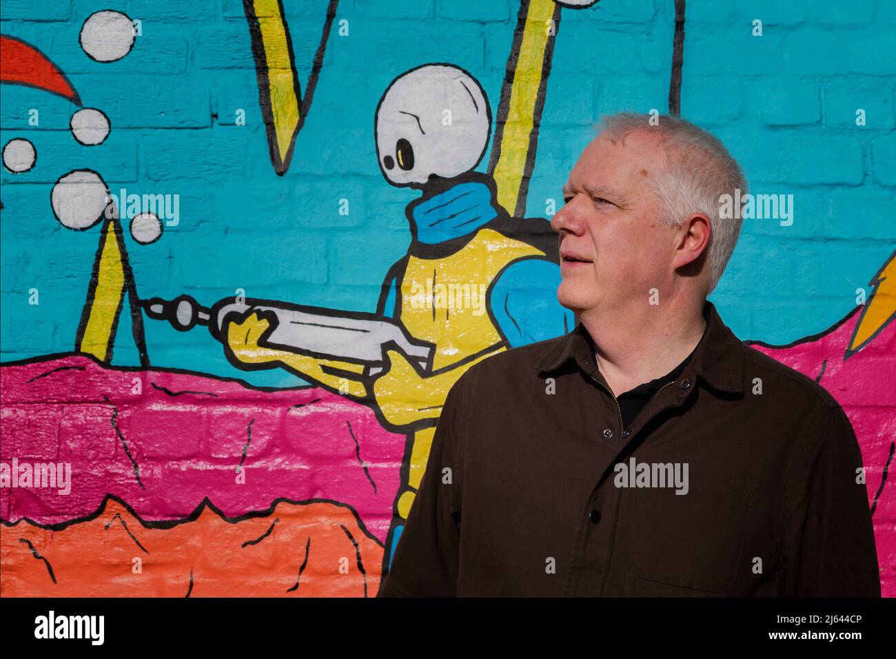 Ein Mann mittleren Alters, der vor einer Wand mit farbenfroher Straßenkunst steht Stockfoto