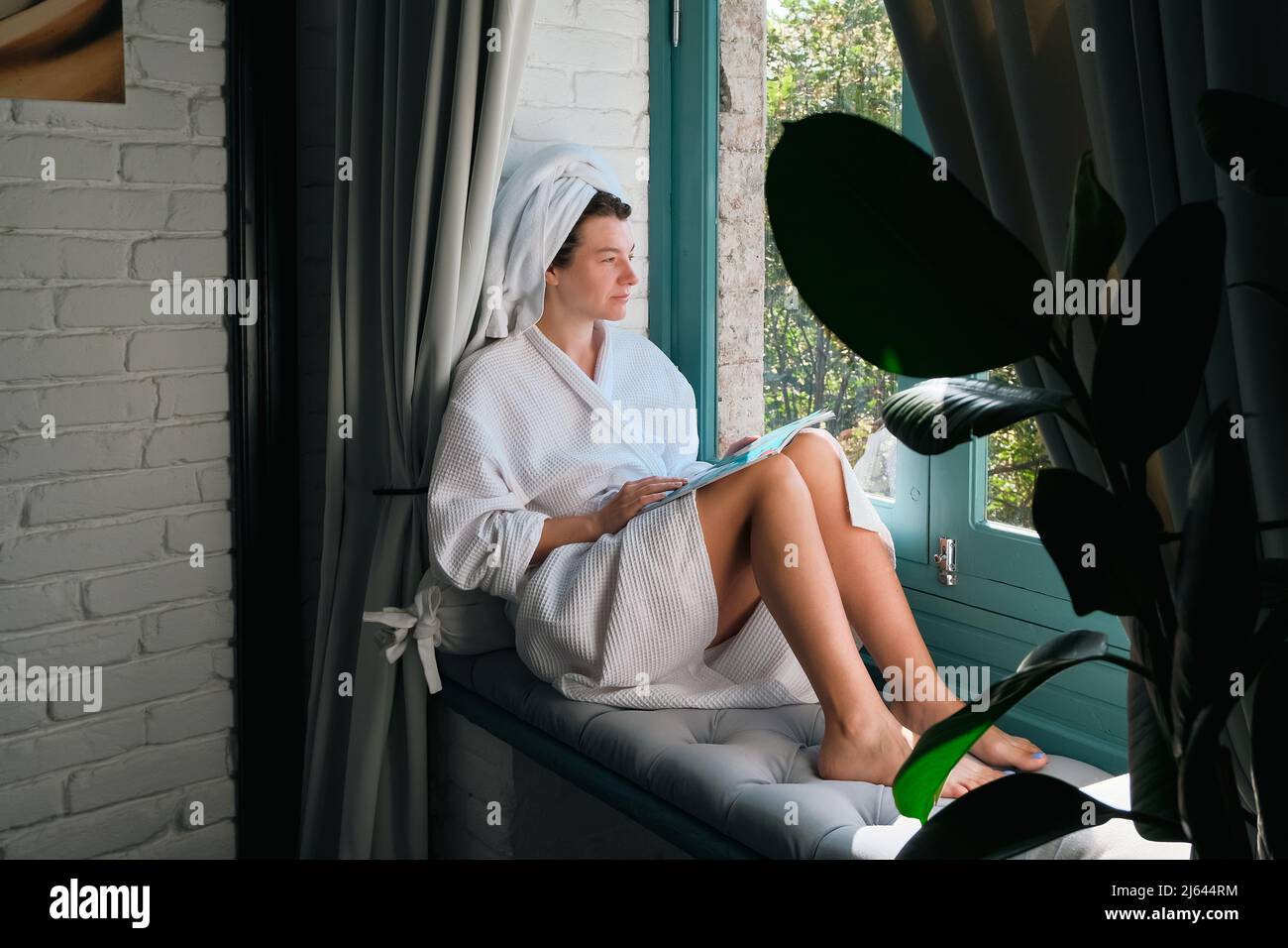 Entspannende Frau nach der Dusche auf dem Fensterbrett sitzend. Wellness, Spa, psychische Gesundheit und Wohlbefinden Konzept. Muttertag oder Frauentag. Stockfoto