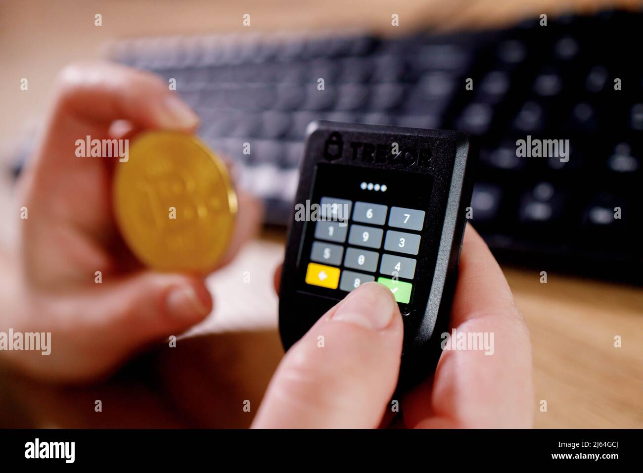 Nahaufnahme Womans Hand hält Bitcoin und cryptocurrencey Hardware kalte Brieftasche auf keybord Hintergrund. Sicherer Kryptowährungsspeicher. Stockfoto