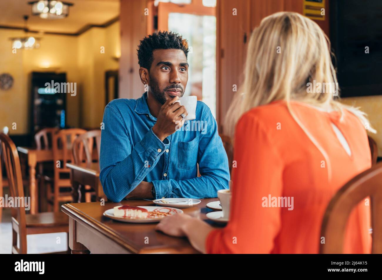 Der kolumbianische Mann hört einer weißen Frau aufmerksam zu, während er Kaffee trinkt Stockfoto