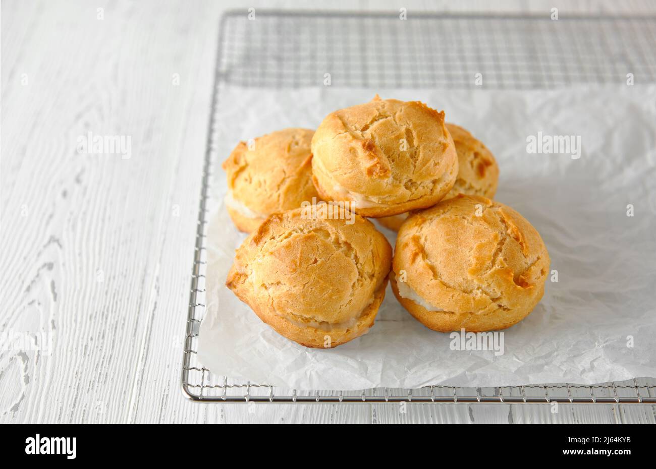 Selbstgemachte Profiterolen oder Eklare auf einem Metallgitter. Traditionelles französisches Dessert. Weißer Holzhintergrund. Nahaufnahme, Kopierbereich. Stockfoto