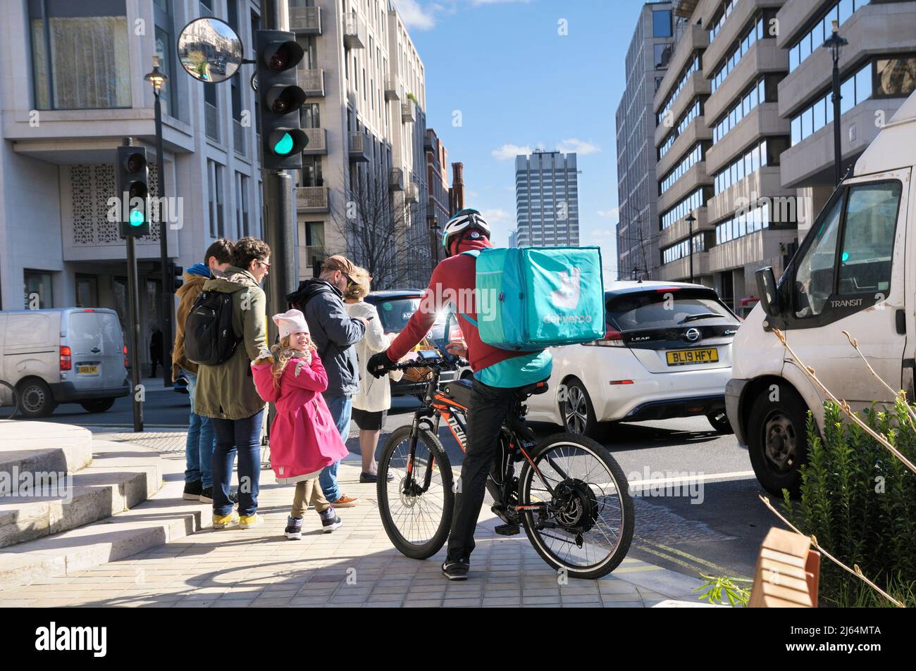 Ein männlicher Deliveroo-Lebensmittelkurier-Radfahrer steht auf seinem Fahrrad in einer Straße mit wärmeisoliertem Rucksack und Logo, im Zentrum von London, England, Großbritannien Stockfoto
