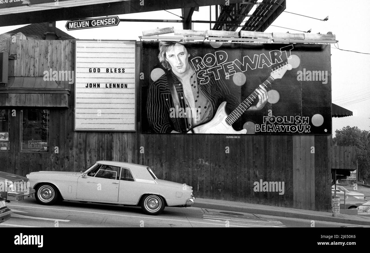 Schild zum Gedenken an den Tod von John Lennon im Jahr 1980 neben einer Plakatwand für Rod Stewart an der Seite des Licorice Pizza Plattenladens am Sunset Strip. Stockfoto