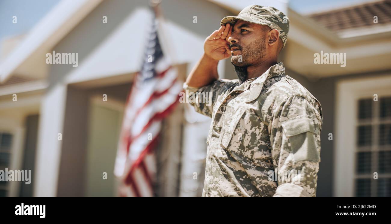Patriotischer junger Soldat, der vor seinem Haus steht, grüßend. Mitglied des United States Marine Corps, das am Veterans Day Ehre und Respekt zeigt. Stockfoto
