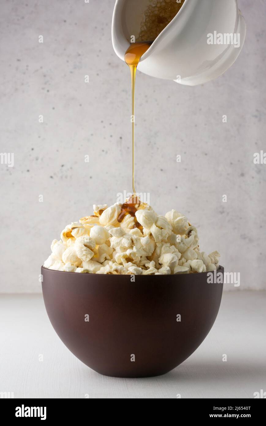 Gießen von Palmzucker-Sirup auf Popcorn, köstlicher, fettarmer, gesunder Snack in einer Tasse, weißer strukturierter Hintergrund, Nahaufnahme Stockfoto