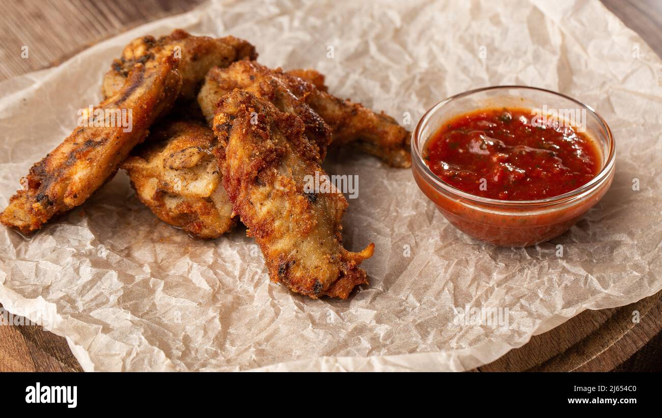 Gebratene Chicken Wings mit echter Hot-BBQ-Sauce, serviert mit roter Chili-Sauce auf einem Pergamentpapier auf Holzhintergrund Stockfoto