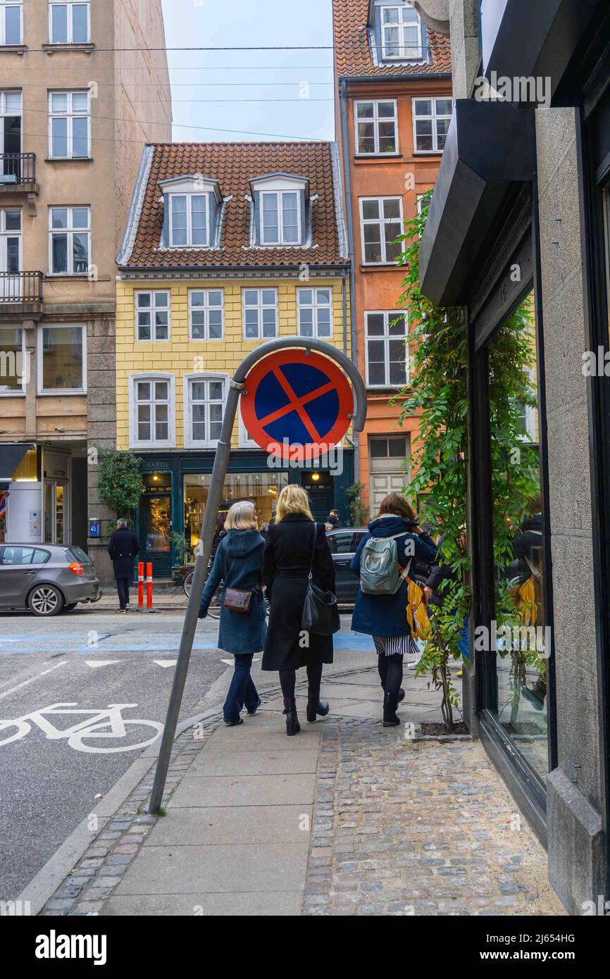 Kopenhagen, Dänemark - 14. November 2021: Ein schiefe Straßenschild für das Verbot von Anhalten und Parken neben dem Bürgersteig und die Frauen, die es auf ihrem passieren Stockfoto