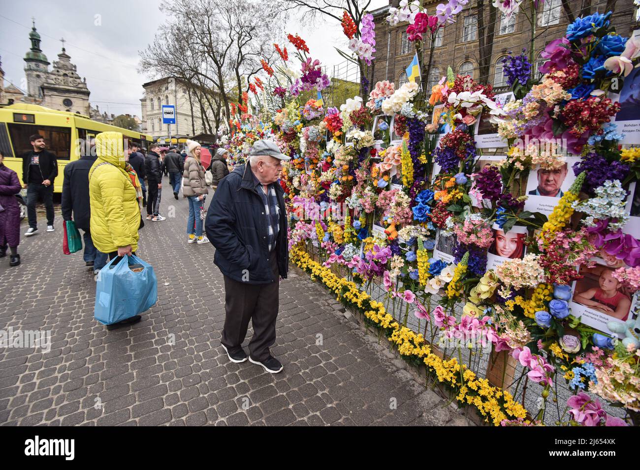 Die Menschen sehen Fotos von Menschen, die von Russen während der russischen Militärinvasion in die Ukraine an der „Mauer der Erinnerung“ in Lemberg getötet wurden. Der Amerikaner Leo Soto, der Gründer der gemeinnützigen Organisation „Wall of Hope“ Foundation, kam eigens in die Ukraine und schuf eine „Wall of Memory“ auf einer der Straßen von Lemberg. Er fand Fotos von russischen Opfern im Internet und druckte sie aus. Er schmückte die Wand mit Fotos von künstlichen Blumen. Auf diese Weise wollte er die unschuldigen Opfer der russischen militärischen Aggression in der Ukraine ehren. Stockfoto