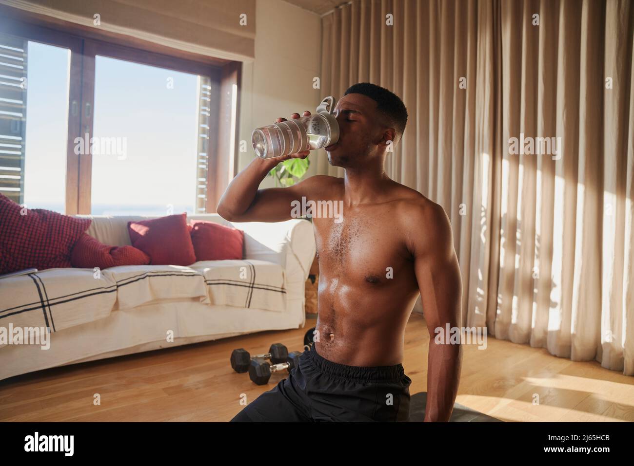 Afroamerikanischer junger schwarzer Mann, der nach dem Training zu Hause in seinem Wohnzimmer Trinkwasser ausübt Stockfoto