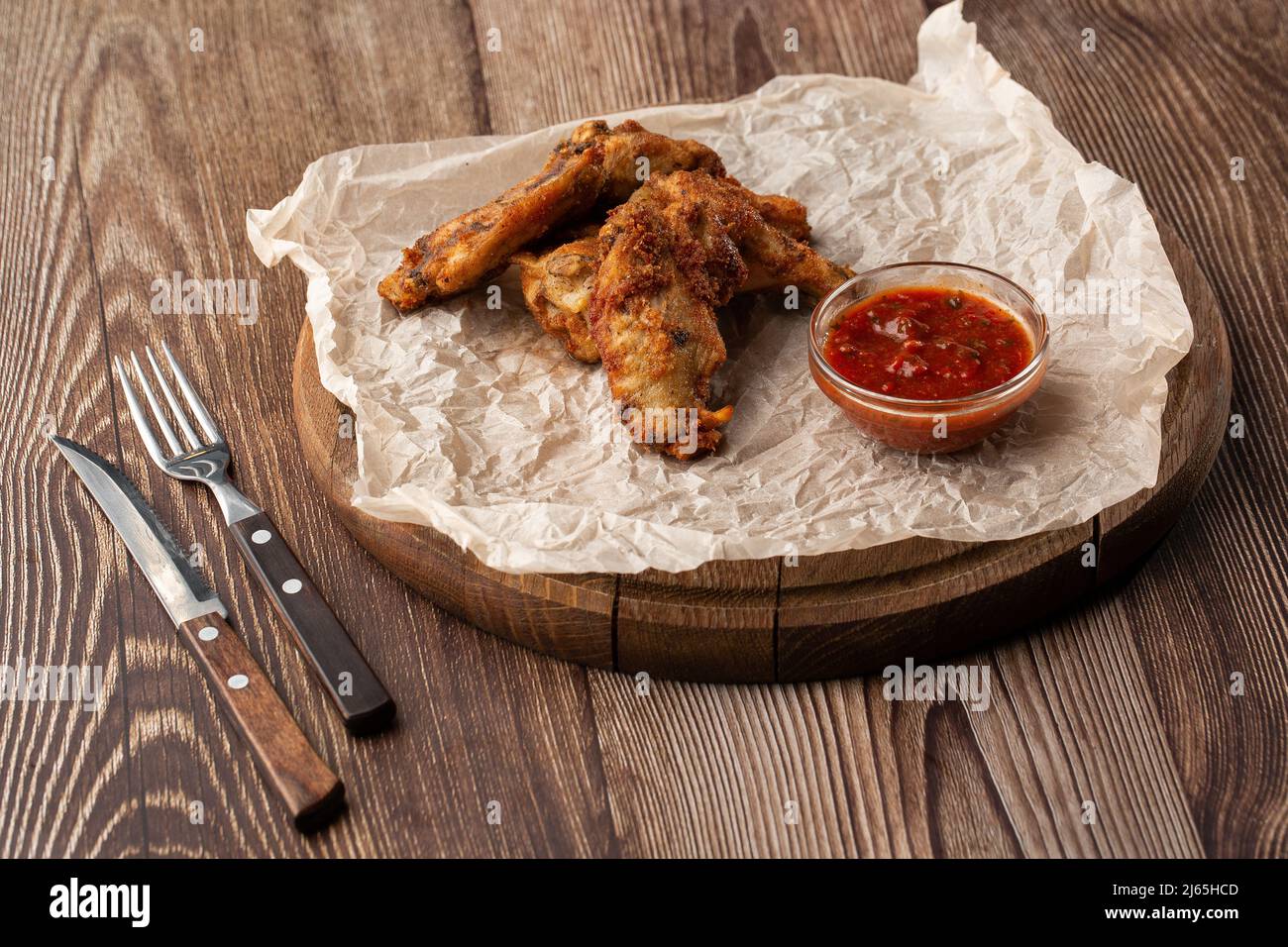 Gebratene Chicken Wings mit echter Hot-BBQ-Sauce, serviert mit roter Chili-Sauce auf einem Pergamentpapier auf Holzhintergrund Stockfoto
