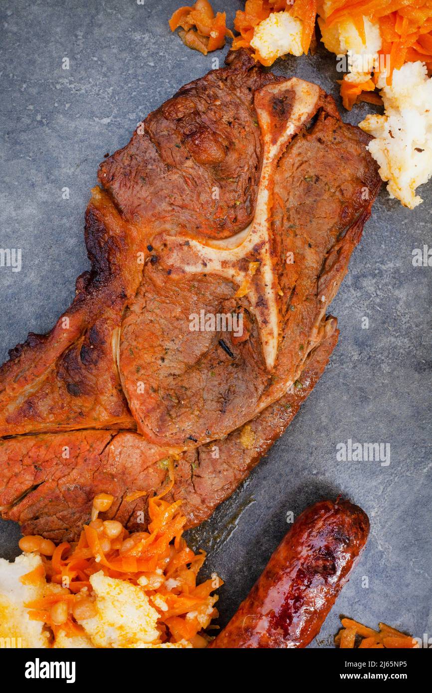 Flaches Lay aus traditionellem südafrikanischem Braai oder Shisa Nyama, auf offener Flamme gekochtes Fleisch und traditionelle Beilage aus Pap und Chakalaka. Stockfoto