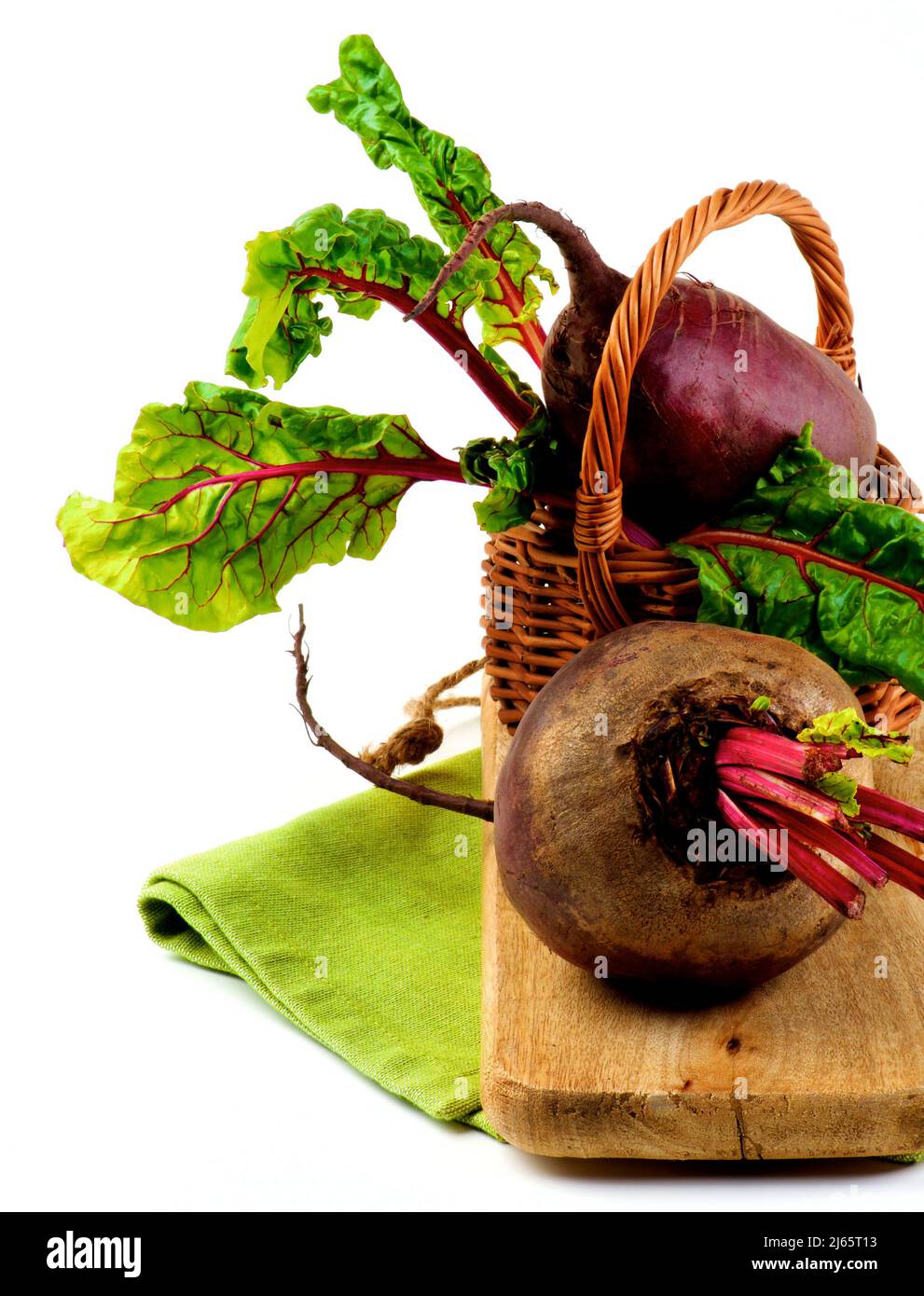 Frische rohe Bio-Rübenwurzeln mit grünen Rübenoberteile im Weidenkorb auf Serviette und Holzbrett Nahaufnahme auf weißem Hintergrund Stockfoto