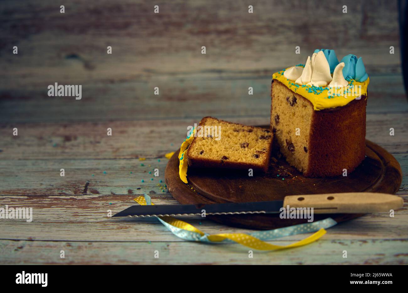 Osterkarte. Osterkuchen mit Creme in den Farben der ukrainischen Flagge und Messer auf einem Holzbrett dekoriert Stockfoto