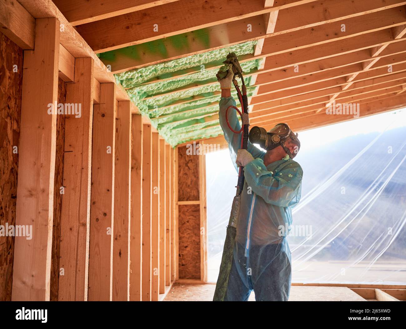 Männlich Baumeister isolierenden Holzrahmen Haus. Mann Arbeiter sprühen Polyurethan-Schaum in der zukünftigen Hütte, mit Plural Komponente Pistole. Bau- und Isolierkonzept. Stockfoto