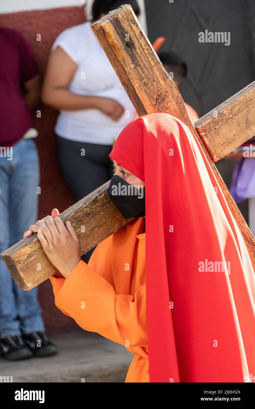 Eine junge Mexikanerin trägt in Kostümen ein Holzkreuz durch die Straßen während einer Prozession zum Karsamstag von der St. Francisco Assisi Kirche am 16. April 2022 in Patzcuaro, Michoacan, Mexiko. Die kleine indigene Stadt bewahrt die Traditionen der spanischen Kolonialherrschaft, einschließlich der Bruderschaft der Büßer während der Karwoche. Stockfoto