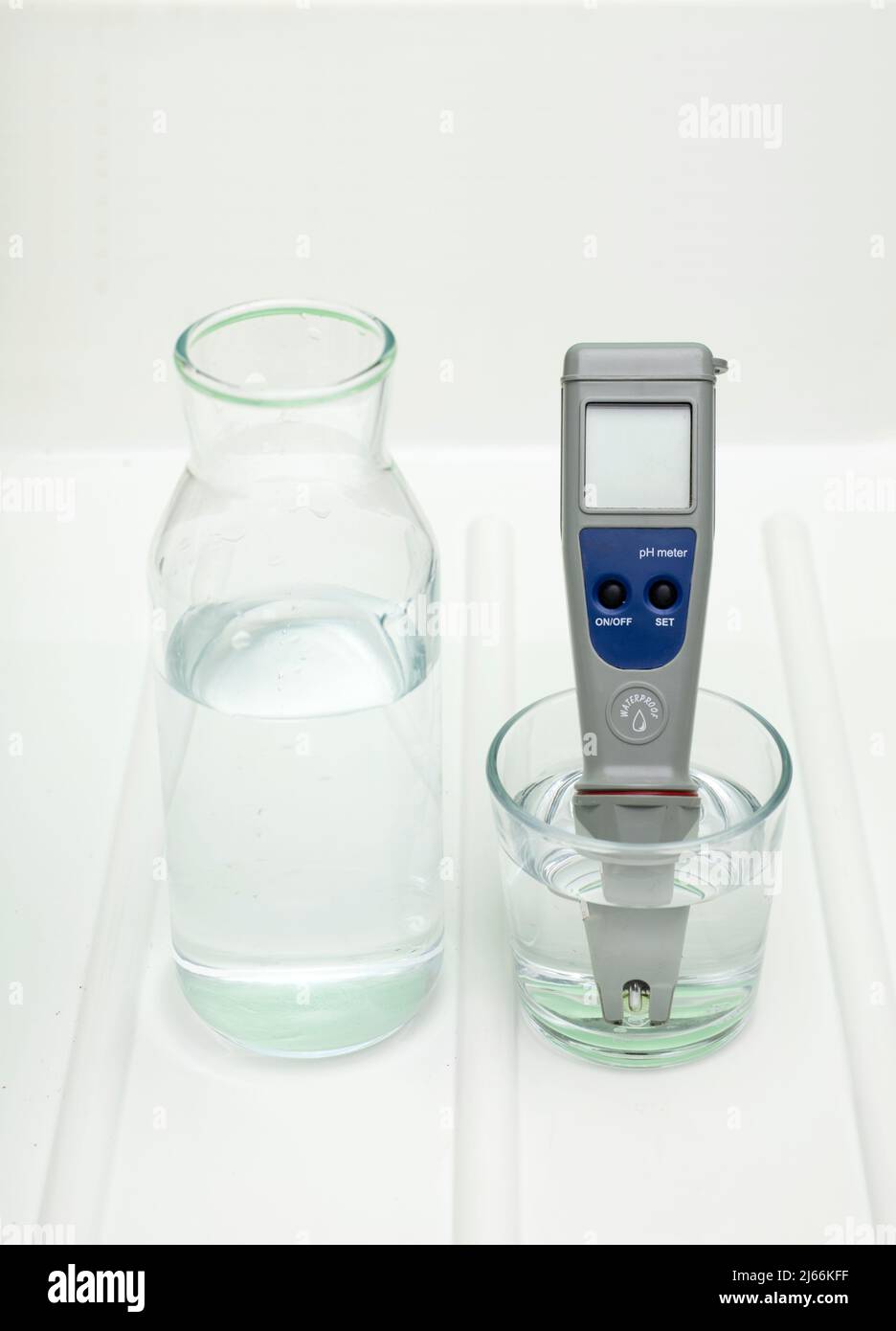 PH-Messgerät in einem Glas Wasser und Flasche auf weißem und grünem Hintergrund. Messung der Eigenschaften von Trinkwasser. Die Härte des wa Stockfoto