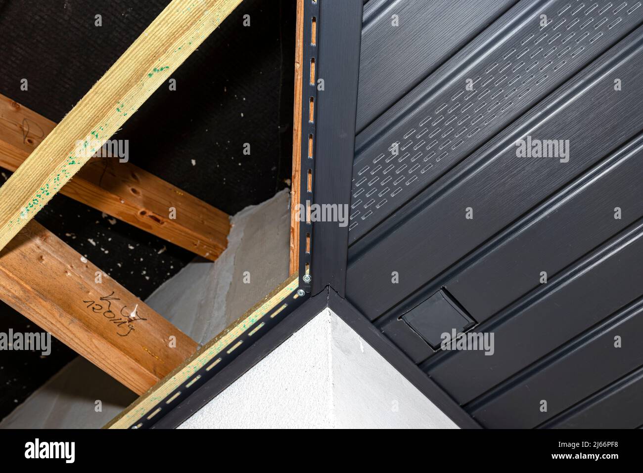 Gerüst mit drei Reihen von Holzlatten und einem modernen Graphitsoffit, sichtbaren H- und J-Lamellen und versteckter Steckdose. Stockfoto
