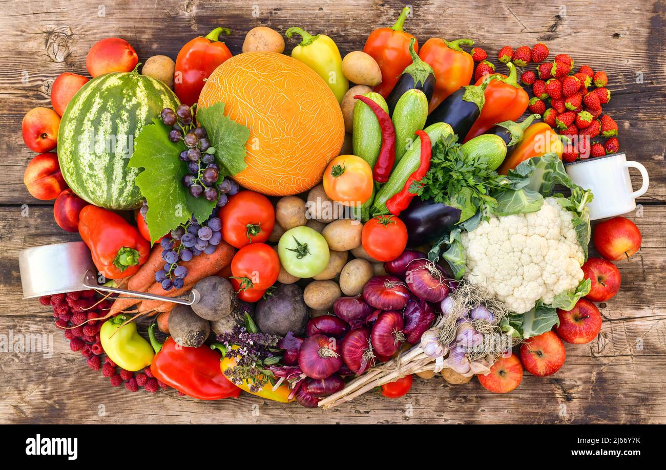 Eine Ernte von Obst, Gemüse und Beeren, gesammelt in einem großen Stapel auf einer hölzernen Arbeitsplatte. Stockfoto