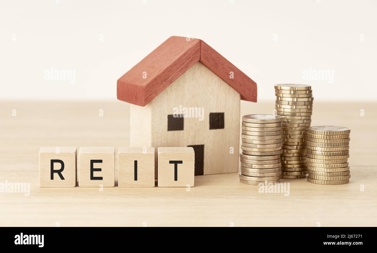 REIT Real Estate Investment Trust Konzept. Hausmodell, Geld und Holzblöcke mit Text Stockfoto