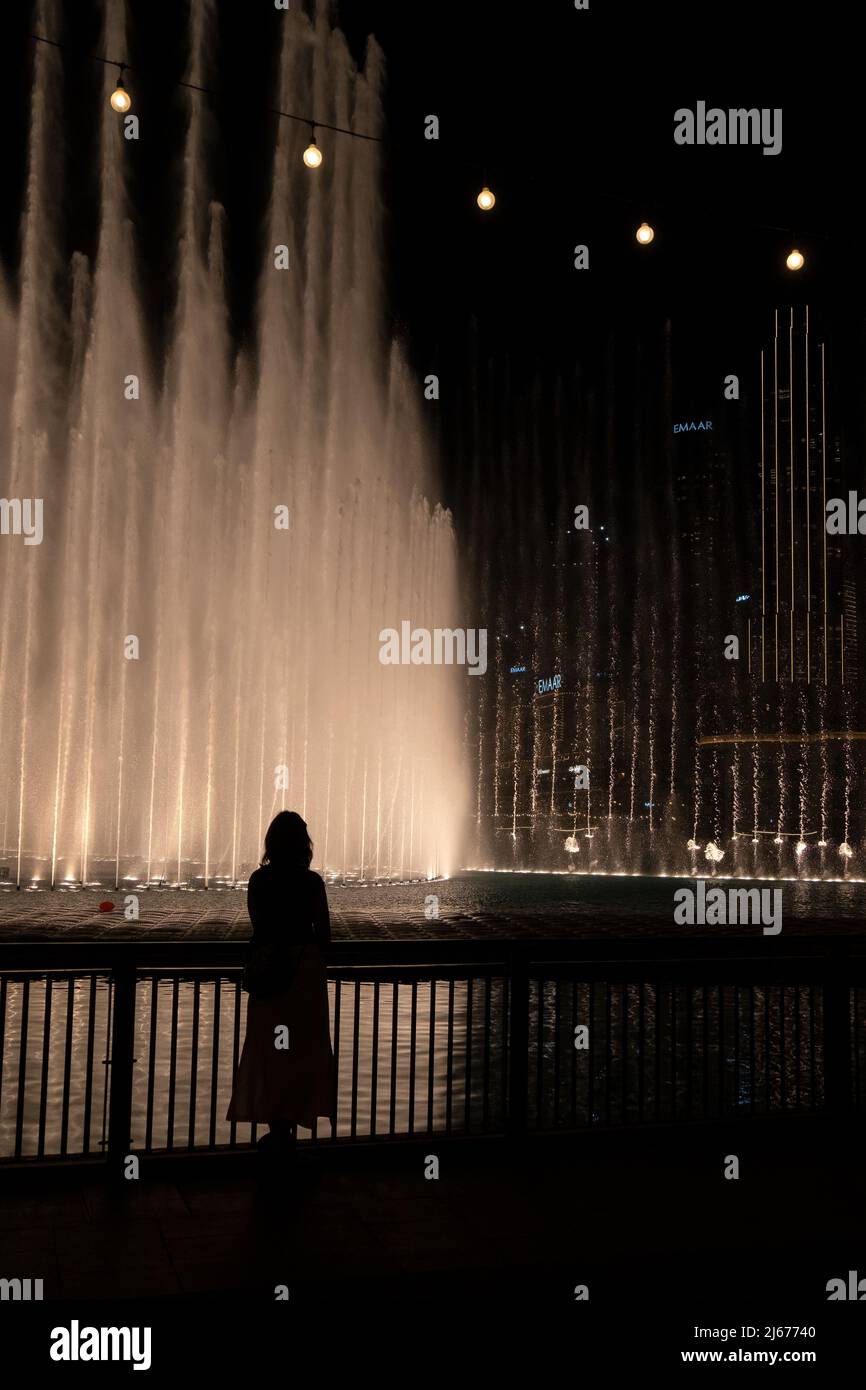 DUBAI, U.A.E - April 20 2022: Silhouette eines jungen Mädchens vor dem Dubai Fountain, aufgenommen am Abend. Dubai, Vereinigte Arabische Emirate Stockfoto