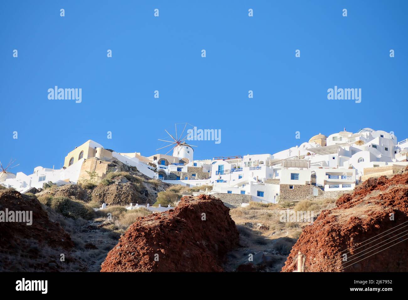 Eine weiß getünchte Windmühle und Hotels mit Balkonen auf der Spitze der vulkanischen Landschaft in Oia Santorini Stockfoto