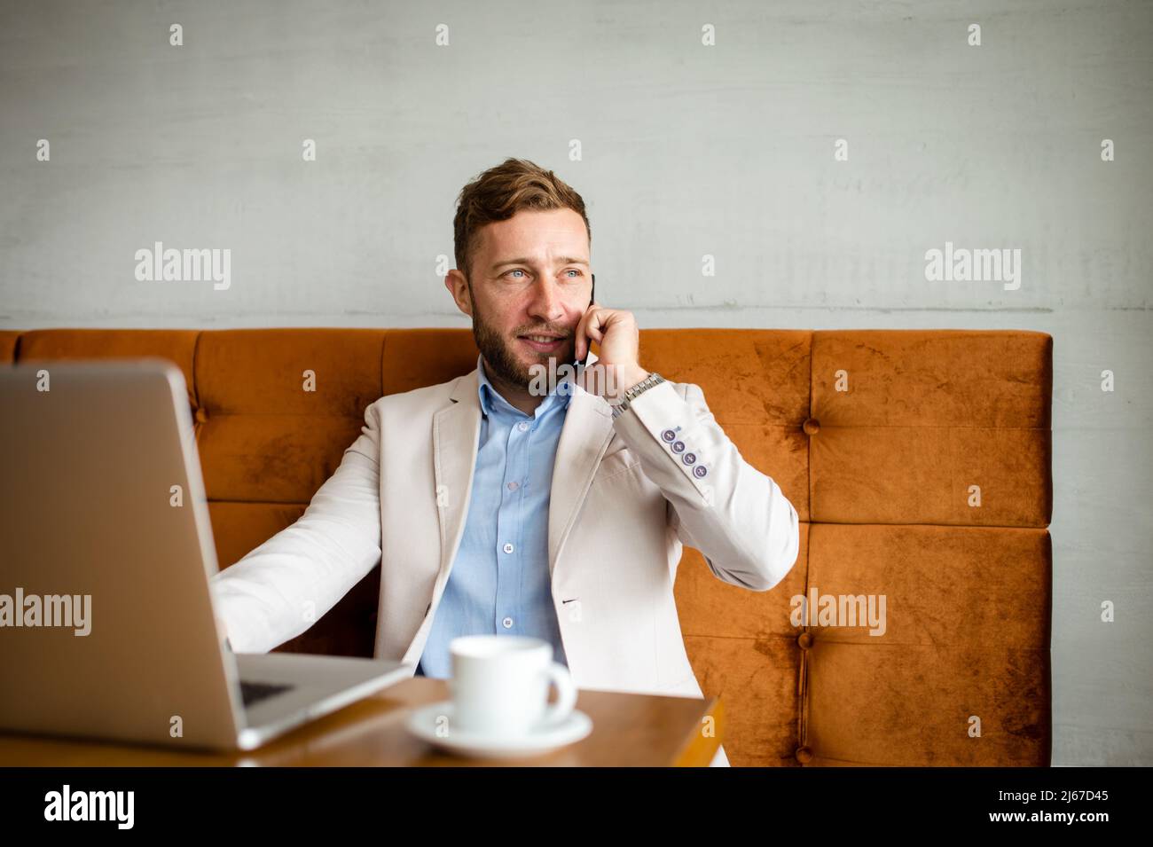 Ein lächelnder Geschäftsmann sitzt in einem Café und telefoniert. Eine neue Arbeitswoche mit vielen Verpflichtungen. Stockfoto