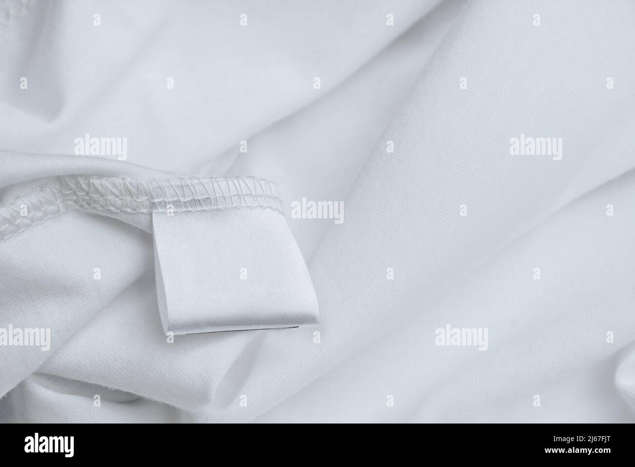 Leeres Etikett für die Zusammensetzung und Beschreibung des Stoffes auf einem Hintergrund mit weißer Bekleidungsstruktur. Kleiderpflege. Stockfoto