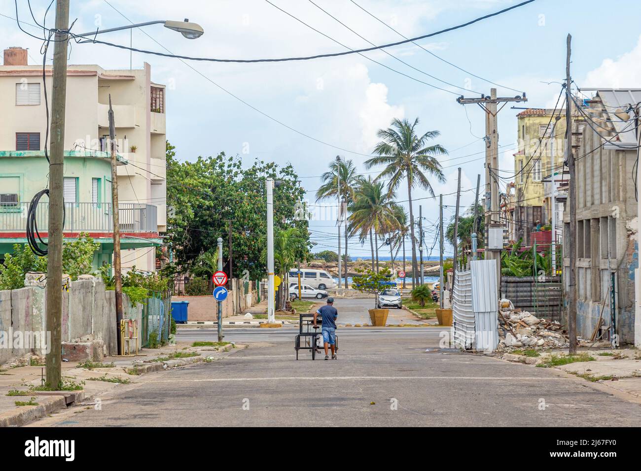 Ein Kubaner schiebt ein Dreirad in einer verlassenen Stadtstraße. In der Ferne können Sie das Küstengebiet der Hauptstadt Meer. Rechts, Schutt in a b Stockfoto