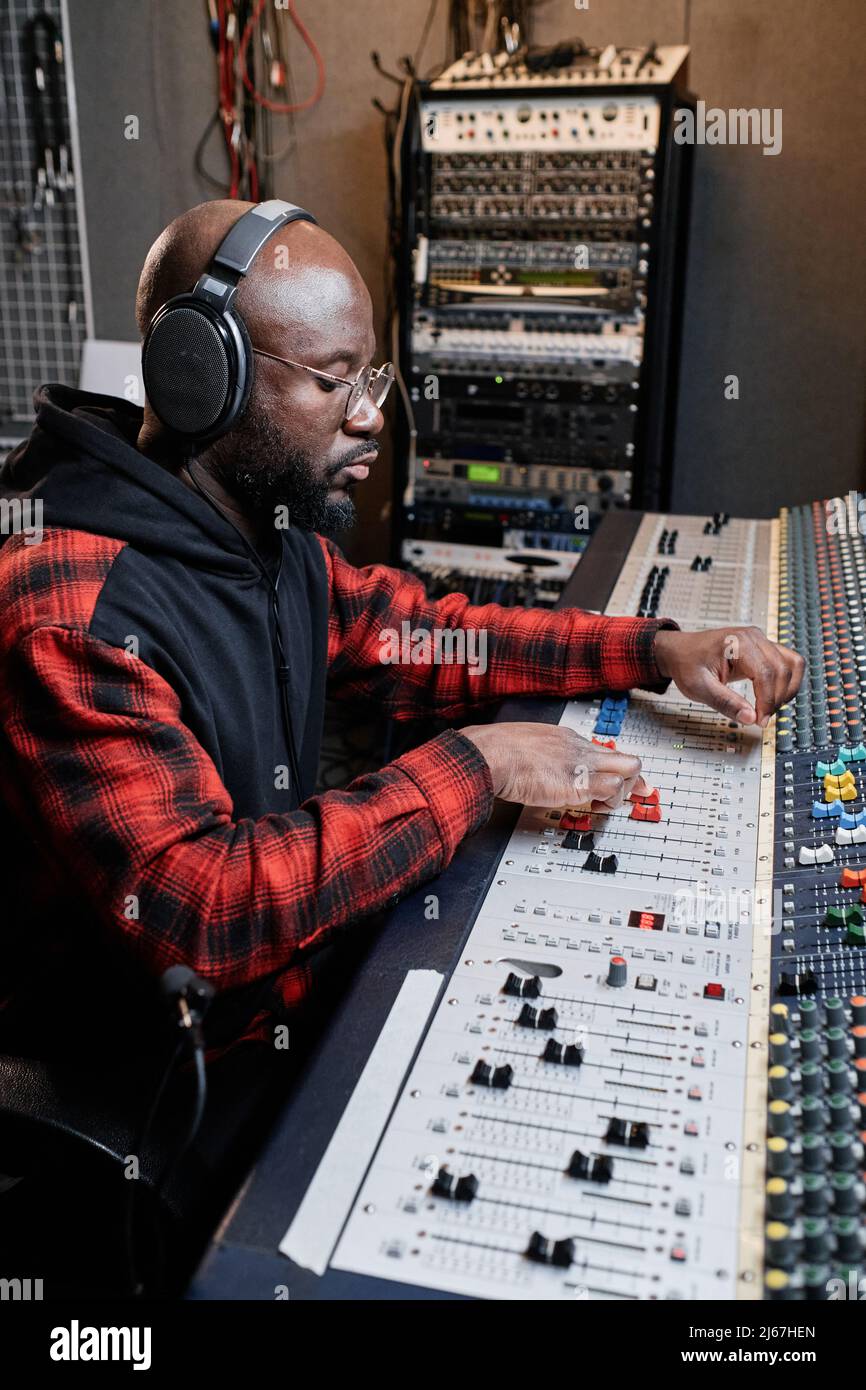 Vertikale Aufnahme eines modernen afroamerikanischen Tontechnikers, der mit einem Mischpult Musik kreiere Stockfoto
