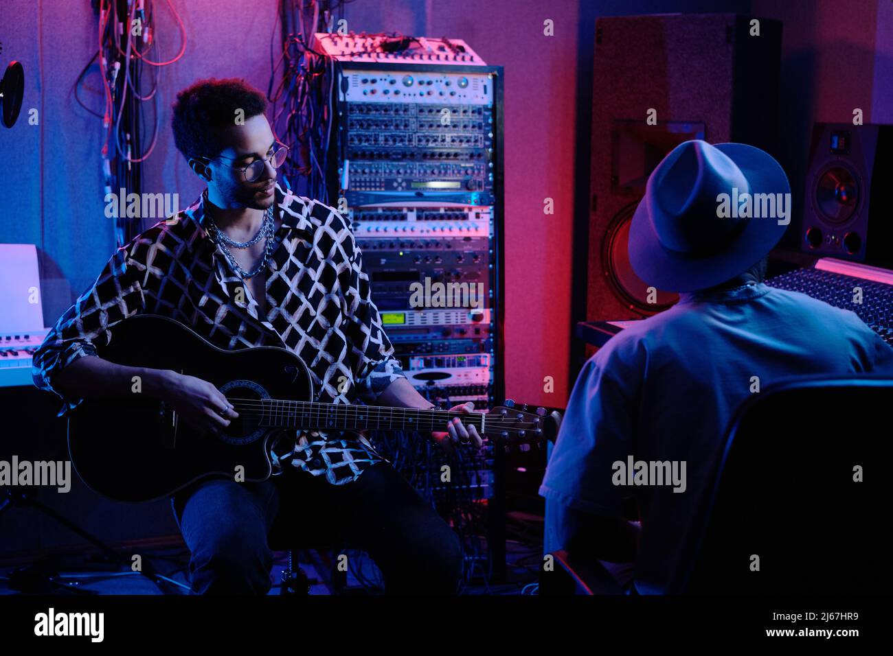 Nicht erkennbarer Audio-Ingenieur und kreativer junger afroamerikanischer Gitarrist, der im Tonstudio am Album arbeitet, Neonbeleuchtung Stockfoto