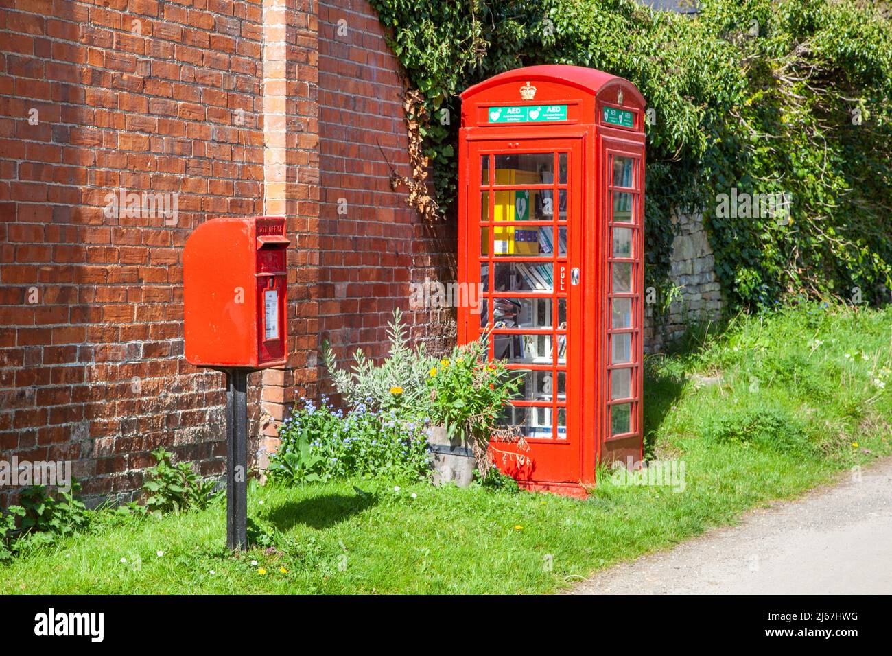 Rote englische Briefkasten und Telefonkiosks werden jetzt als Bücheraustausch genutzt und enthalten den Dorf-Defibrillator im Weiler Grafton Worcestershire Stockfoto