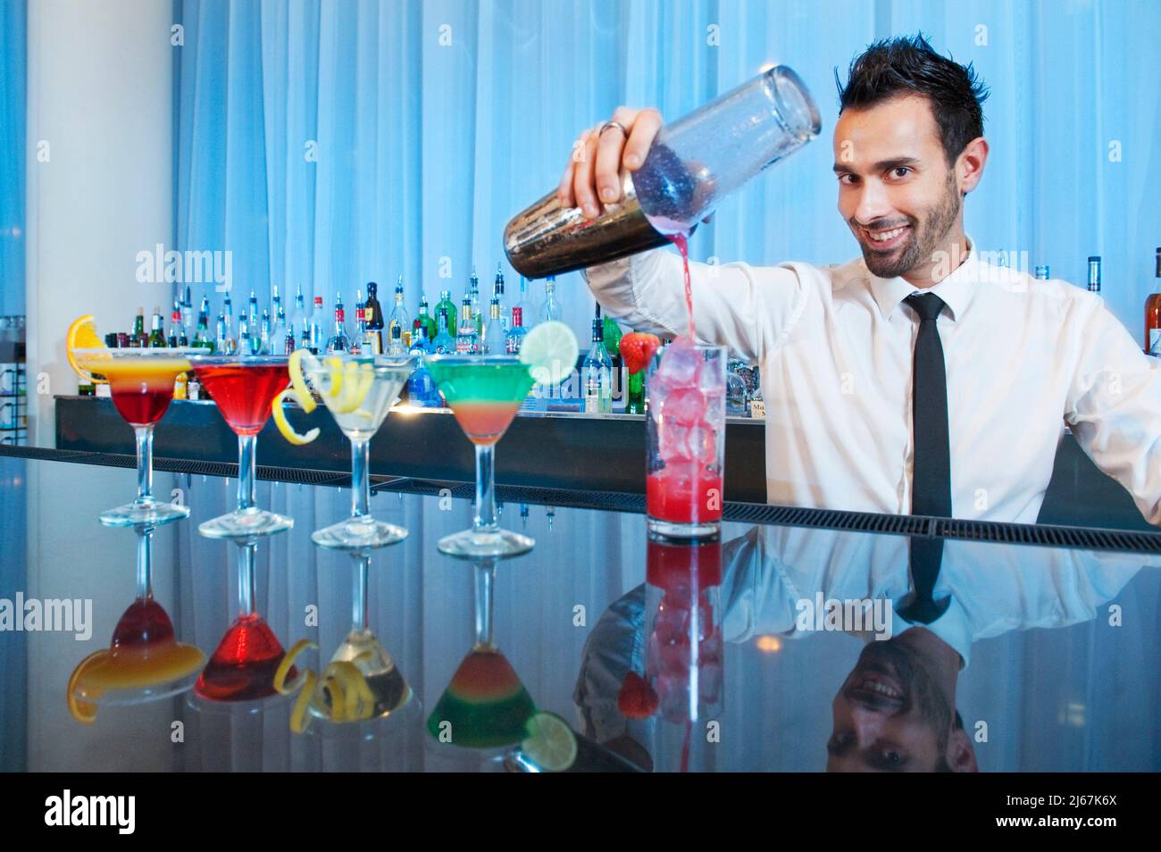 Der Barkeeper lächelt der Kamera zu, während er Getränke gießt. Stockfoto