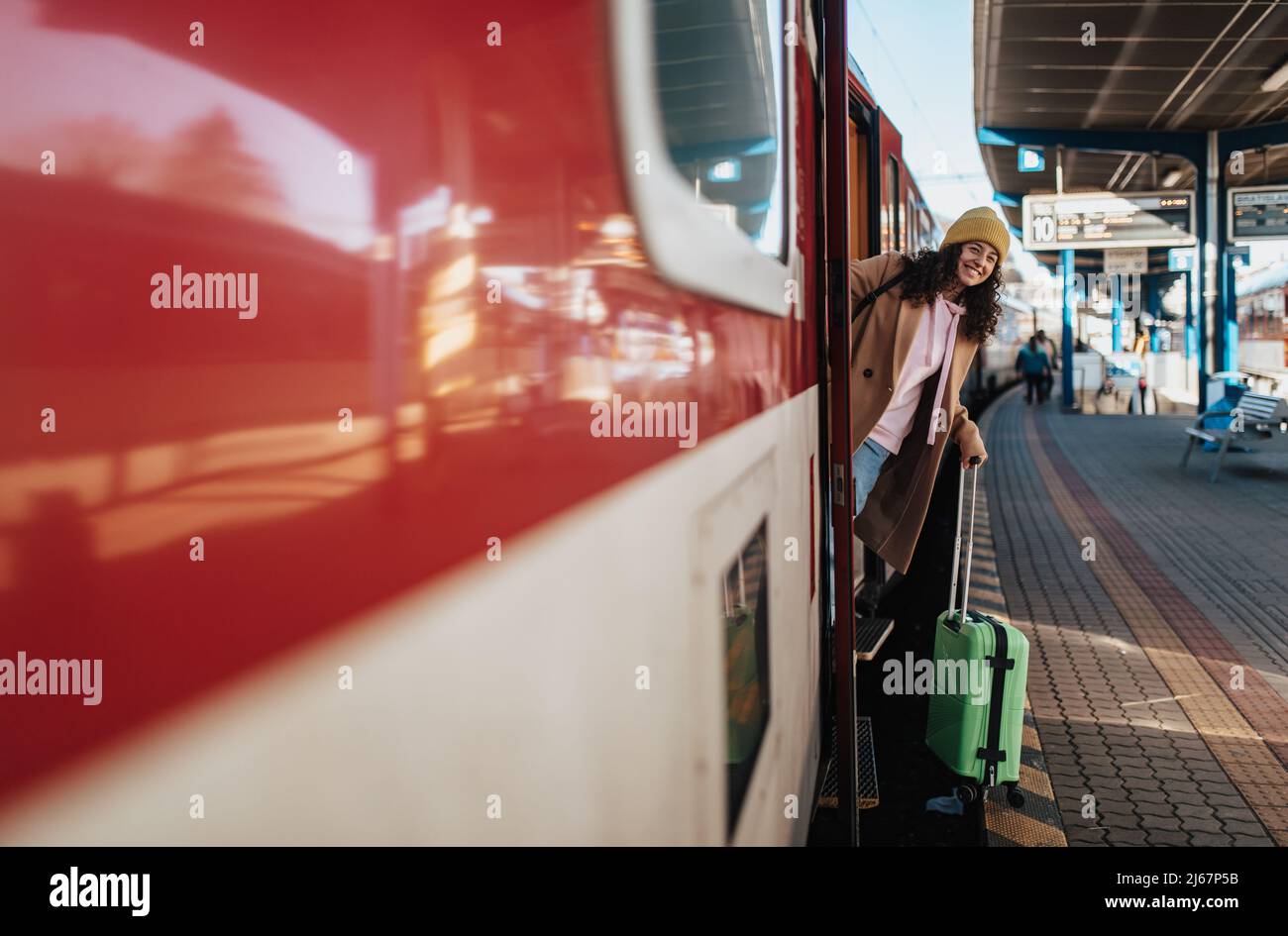 Glückliche junge Reisende Frau mit Gepäck, die am Bahnhofsplatz aus dem Zug aussteigen Stockfoto
