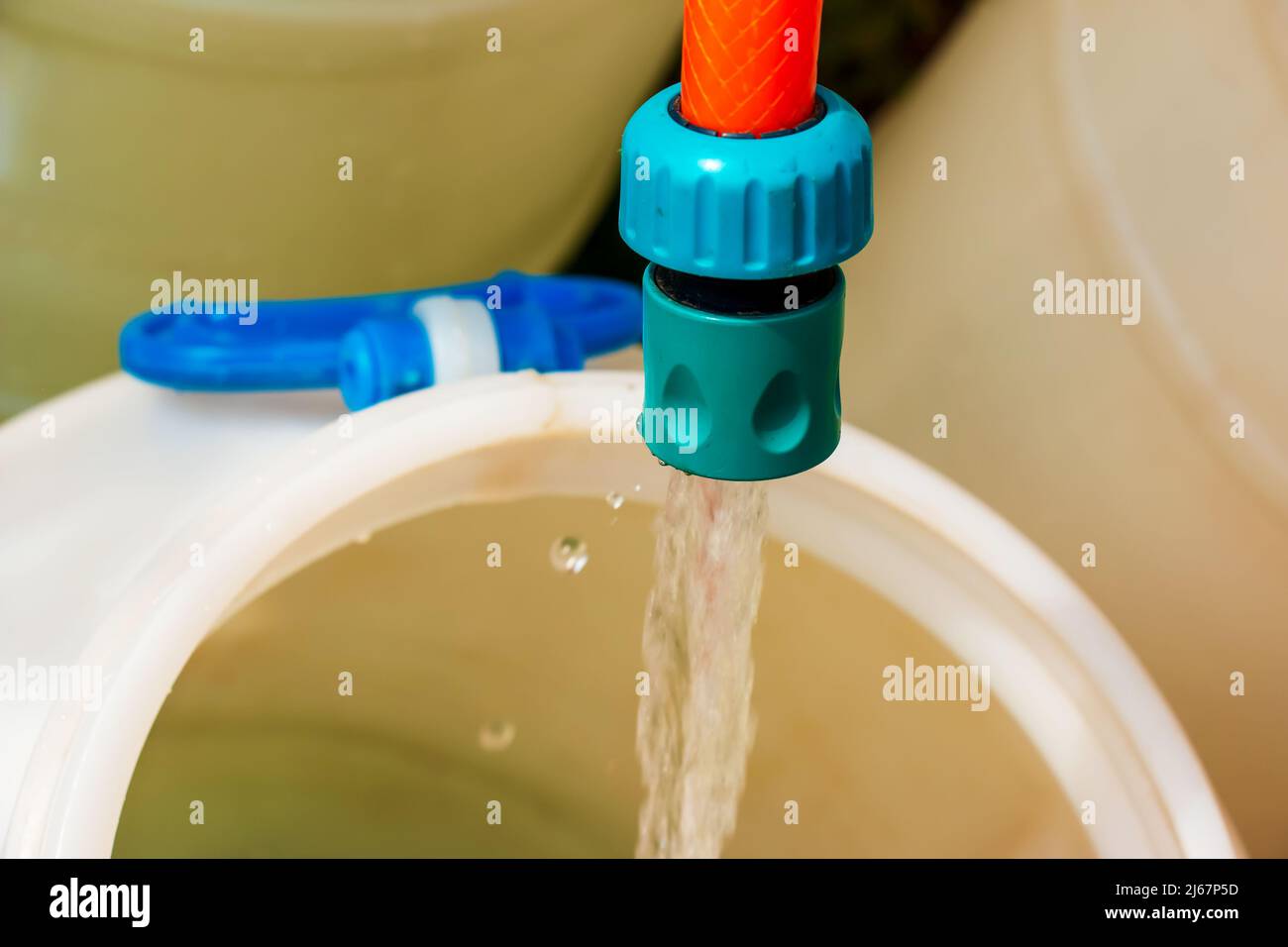 Ein Wasserstrahl aus einem Schlauch füllt ein Kunststofffass. Hintergrundbild. Das Konzept der Trinkwasserkrise in der Welt. Stockfoto