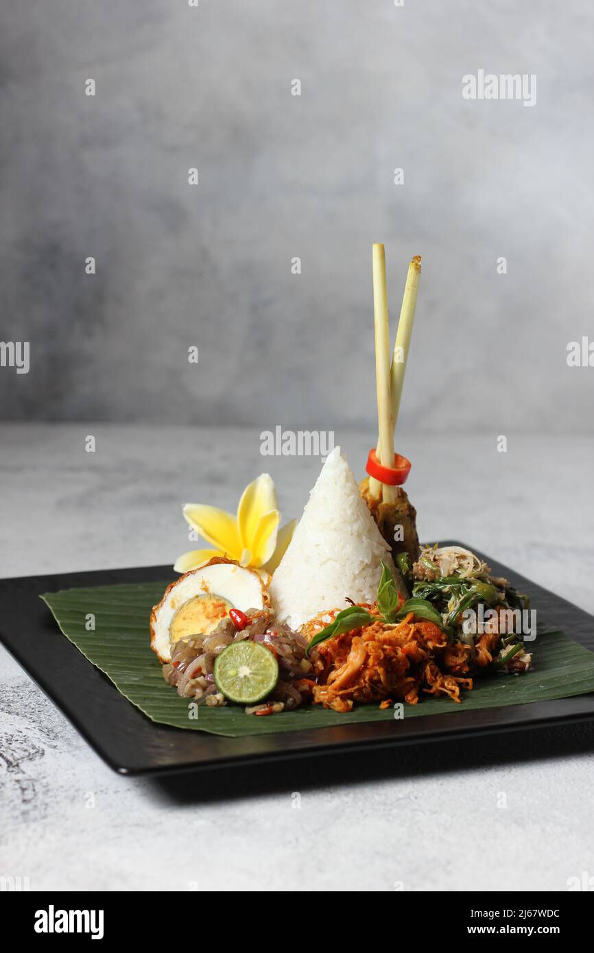 Leckere würzige Nasi bali mit Chili-Ei, Hühnersatay und Salat-Gemüse auf schwarzem, tellweißem Hintergrund Stockfoto