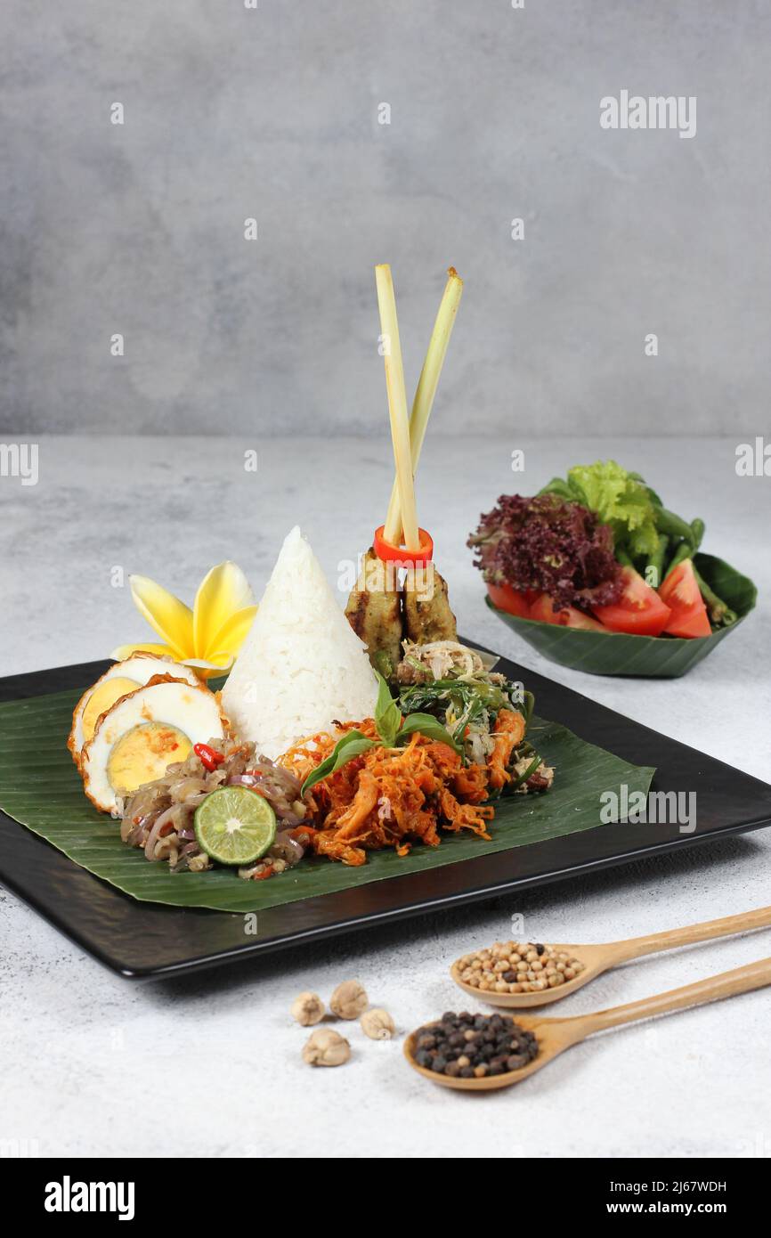 Leckere würzige Nasi bali mit Chili-Ei, Hühnersatay und Salat-Gemüse auf schwarzem, tellweißem Hintergrund Stockfoto