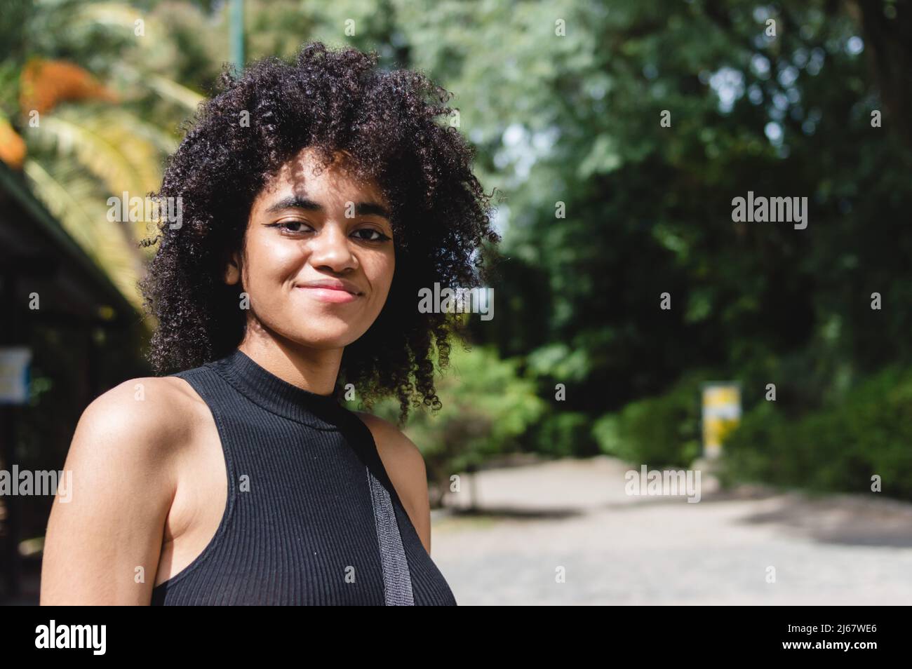 Portrait junge Brünette Frau mit Afro im Urlaub im Freien in einem Naturpark, Blick auf die Kamera lächelnd. Stockfoto