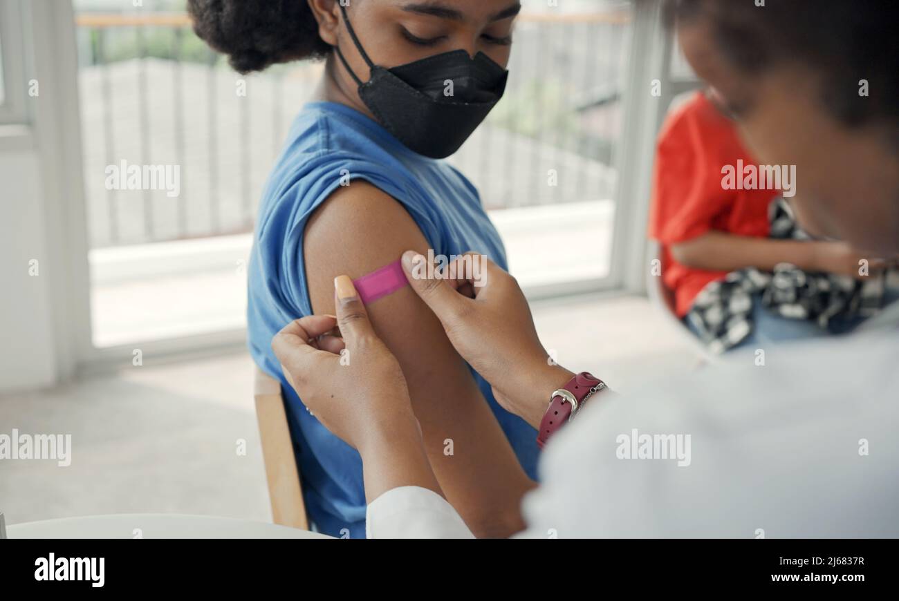 Der afroamerikanische Arzt trägt nach der Impfung Gips auf die Schulter eines Kindes auf. Öffnen Sie die Ärmel, um bei der Heilung gegen Grippe oder Epidemie zu impfen Stockfoto