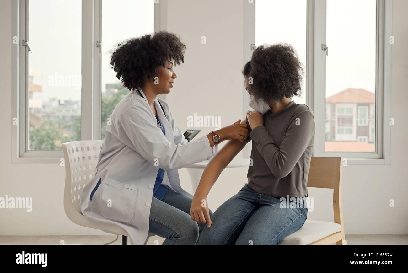 Der afroamerikanische Arzt trägt nach der Impfung Gips auf die Schulter eines Kindes auf. Öffnen Sie die Ärmel, um bei der Heilung gegen Grippe oder Epidemie zu impfen Stockfoto